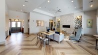 This thoughtfully designed single-floor community space blends modern aesthetics with comfortable functionality. The open-concept layout is anchored by striking herringbone-patterned hardwood flooring that flows seamlessly throughout. The main lounge area features a dramatic floor-to-ceiling stacked-stone accent wall housing a sleek linear fireplace, creating a warm and inviting focal point. Generous ceiling heights, tray ceiling details, and recessed lighting contribute to the spacious, airy atmosphere, while a ceiling fan adds a practical touch.

Adjacent to the lounge is a well-appointed kitchen outfitted with gray shaker-style cabinetry, marble-look countertops, stainless steel appliances, and a classic white subway tile backsplash. A curved, stone-clad island with bar seating serves as a central gathering spot, complemented by pendant lighting overhead. A beverage station with hexagonal tile detailing adds a distinctive design element nearby.

Large windows and glass doors frame views of a resort-style pool and outdoor amenity area, flooding the interior with natural light. Intimate bistro seating near the windows offers a relaxed setting to enjoy the outdoor scenery. Throughout the space, the combination of natural textures, contemporary furnishings, and curated décor creates a welcoming and upscale communal environment.