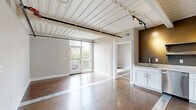 Located at 2150 Byrum Ave in Nashville, TN, this 2-bedroom, 2-bathroom unit offers a distinctive industrial aesthetic blended with modern finishes. The space is characterized by its striking exposed beam ceilings with corrugated metal panels painted white, creating an open, loft-like ambiance throughout.

The kitchen is well-appointed with stainless steel appliances, including a French door refrigerator, electric range, built-in microwave, and dishwasher. White shaker-style cabinetry is complemented by open metal shelving and white countertops against an olive-toned accent wall, adding warmth to the space. Rich hardwood flooring flows throughout the unit.

Both bedrooms are generously proportioned, featuring soft gray walls, hardwood floors, and large windows that fill the rooms with natural light and offer views of the surrounding Nashville neighborhood. The primary bedroom is a comfortable size with ample wall space.

Each bathroom is finished with white shaker vanity cabinets, white countertops, large mirrors with bar lighting, and clean, neutral tiling — delivering a crisp, modern feel. A dedicated closet provides practical storage. The unit's industrial character, modern upgrades, and natural light make it a compelling offering in Nashville's vibrant Byrum Ave corridor.