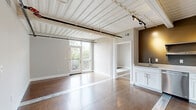 Located at 2150 Byrum Ave in Nashville, TN, this 2-bedroom, 2-bathroom unit offers a distinctive industrial aesthetic blended with modern finishes. The space is characterized by its striking exposed beam ceilings with corrugated metal panels painted white, creating an open, loft-like ambiance throughout.

The kitchen is well-appointed with stainless steel appliances, including a French door refrigerator, electric range, built-in microwave, and dishwasher. White shaker-style cabinetry is complemented by open metal shelving and white countertops against an olive-toned accent wall, adding warmth to the space. Rich hardwood flooring flows throughout the unit.

Both bedrooms are generously proportioned, featuring soft gray walls, hardwood floors, and large windows that fill the rooms with natural light and offer views of the surrounding Nashville neighborhood. The primary bedroom is a comfortable size with ample wall space.

Each bathroom is finished with white shaker vanity cabinets, white countertops, large mirrors with bar lighting, and clean, neutral tiling — delivering a crisp, modern feel. A dedicated closet provides practical storage. The unit's industrial character, modern upgrades, and natural light make it a compelling offering in Nashville's vibrant Byrum Ave corridor.