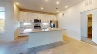 This modern single-floor residence offers a well-designed, open-concept layout that seamlessly connects the living and kitchen areas. The kitchen is a standout feature, equipped with stainless steel appliances including an electric range, over-the-range microwave, and a French door refrigerator. Crisp white cabinetry with sleek black hardware lines the walls from counter to ceiling, complemented by a generous center island with a light quartz countertop and an integrated sink — ideal for both meal preparation and casual dining. Polished concrete floors extend throughout the main living area, adding an industrial-modern touch, while large sliding glass doors and multiple windows flood the space with natural light and provide direct access to a private balcony overlooking a tree-lined streetscape. The bedrooms feature plush carpeting and large windows that frame greenery and neighborhood views, creating comfortable, light-filled retreats. The primary bathroom is appointed with a dual-sink vanity, white quartz countertops, a full tub-shower combination with white subway tile, and recessed lighting. A secondary bathroom mirrors the clean, all-white aesthetic. A dedicated laundry room with a full-size washer and dryer and built-in shelving adds everyday convenience to this thoughtfully designed residence.