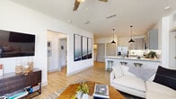 This thoughtfully designed 2-bedroom, 2-bathroom residence offers a comfortable and modern living experience across a single floor. The open-concept living and kitchen area serves as the heart of the home, featuring light hardwood flooring, neutral white walls, and abundant natural light from large windows dressed with elegant draping. The kitchen is equipped with full-height gray shaker-style cabinetry, white quartz countertops, stainless steel appliances including a refrigerator, range, microwave, and dishwasher, and a peninsula island illuminated by sleek pendant lighting — ideal for both cooking and casual dining. The living area flows seamlessly from the kitchen, offering a relaxed, open ambiance with a ceiling fan overhead. The spacious primary bedroom features plush carpet flooring, a ceiling fan, and a large window with outdoor views. It includes a generously sized walk-in closet with built-in shelving and hanging rods. The second bedroom is equally well-lit with views to the exterior. Both bathrooms are finished with gray shaker vanities, white countertops, large framed mirrors, and wood-look tile flooring. A dedicated laundry room and hallway complete the layout, making this a highly functional and stylish residence.
