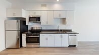 Located on Wilshire Boulevard in the heart of Los Angeles, this single-floor unit offers a clean, modern aesthetic defined by an open-concept layout and abundant natural light. Light-toned hardwood-style flooring runs seamlessly throughout, creating a cohesive and airy feel across all living areas.

The kitchen is thoughtfully designed with white shaker cabinetry, dark countertops, and a full suite of stainless steel appliances, including a gas range, microwave, dishwasher, and refrigerator. A double-basin sink with a modern faucet anchors the workspace, while ample upper and lower cabinetry provides generous storage.

The open living area flows naturally from the kitchen, bathed in natural light from a large window that offers views of the surrounding neighborhood. Recessed lighting and crisp white walls enhance the bright, contemporary atmosphere throughout.

The bedroom is a serene, well-proportioned space featuring a sliding-door walk-in closet and the same warm flooring found throughout the unit. The bathroom is finished with floor-to-ceiling white subway tile surrounding a soaking tub and shower combination, fitted with brushed nickel fixtures for a polished, modern touch.

The entry hallway provides a defined transition into the living space, complete with a bold dark front door and panel box access. Overall, the unit delivers a streamlined, functional design well-suited to urban living in Los Angeles.
