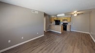 This single-story unit is designed with a practical, open layout that connects the living area directly to the kitchen, creating a cohesive and functional common space. The living area features wood-look vinyl flooring, neutral gray walls, a textured ceiling, and a ceiling fan with a light fixture, contributing to a comfortable and well-lit environment. The kitchen is equipped with light oak cabinetry offering generous storage, laminate countertops, a peninsula with a double-basin sink, and black appliances including a refrigerator, electric range, and under-cabinet range hood. The peninsula layout allows for easy interaction between the kitchen and living space.

The bedrooms feature wall-to-wall carpet and neutral gray walls, each with a window fitted with horizontal blinds that allow natural light while maintaining privacy. Both rooms offer a quiet, functional space suitable for rest or work.

The bathroom includes a wide vanity with a single-basin sink, light oak cabinetry, laminate countertops, and a large mirror with overhead lighting. A separate water closet houses the toilet and a full shower-tub combo with a small window for natural light. Wood-look vinyl flooring extends throughout the bathroom, tying the space together cohesively.