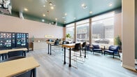 Located at 1412 Seymour Street in Halifax, Nova Scotia, the Bestie Study Lounge is a well-appointed single-floor space designed to serve as a productive and comfortable environment for studying and socializing. The interior is defined by a striking teal-painted ceiling that contrasts warmly with soft blush-toned walls, creating a modern and inviting aesthetic throughout.

The main area is flooded with natural light through large floor-to-ceiling windows along the street-facing wall, offering open views of the surrounding neighbourhood. Light wood-toned flooring runs throughout, complementing the space's clean, contemporary design. A mix of high-top communal tables with bar-height chairs and casual lounge seating with navy blue armchairs provides flexible arrangements to suit both focused work and relaxed conversation.

Along one wall, a built-in service counter branded with the "Bestie" logo serves as a refreshment station, complete with a sink, coffee equipment, and countertop appliances. Adjacent to it, vending machines offer convenient access to snacks and beverages. A secondary, quieter area features standard-height tables lined along a tiled wainscoted wall with warm accent lighting, ideal for heads-down study sessions. A wall-mounted HVAC unit ensures year-round comfort. Recessed ceiling lighting throughout keeps the space bright and well-lit at all hours.