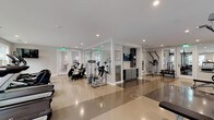 This single-floor fitness center at 2599 Evans Rd in Morrisville, NC, is thoughtfully designed to support a wide range of workout routines. The space is bright and open, featuring polished concrete flooring throughout the main exercise areas, recessed lighting, and large windows that flood the facility with natural light and provide views of the surrounding community.

The cardio zone is generously appointed with multiple treadmills, elliptical machines, and a recumbent bike, all positioned to take advantage of the natural light from the oversized windows. A central hub area features built-in storage cabinetry and a mounted display screen, providing a convenient station between workout zones.

The strength training area is well-stocked with a full power rack, adjustable bench, a comprehensive dumbbell rack, kettlebells in various weights, and additional cable and resistance machines. Floor-to-ceiling mirrors line portions of the walls, enhancing the sense of space and allowing users to monitor their form.

A dedicated studio room, finished with patterned carpet tiles, offers a softer surface ideal for functional training. This area is equipped with TRX suspension trainers mounted to the walls, a ballet barre with mirrored walls, and a rack of medicine balls, making it suitable for barre classes, stretching, and bodyweight exercises. Glass-paneled doors connect the various zones, creating a cohesive and accessible layout throughout the facility.