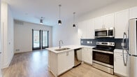 This well-designed one-bedroom, one-bathroom unit offers a thoughtfully laid-out floor plan that maximizes every square foot. The open-concept kitchen and living area serves as the heart of the space, featuring warm wood-look flooring, crisp white walls, and a ceiling fan that keeps the area bright and comfortable. The kitchen is a standout, outfitted with white shaker cabinetry, a blue-gray subway tile backsplash, sleek quartz countertops, a peninsula with an undermount sink, and a full suite of stainless steel appliances including a range, microwave, dishwasher, and refrigerator. Pendant lighting above the peninsula adds a modern touch. French doors at the end of the living area invite natural light and offer views of the surrounding exterior. The bedroom is carpeted for comfort, featuring a large window with views of the neighboring cityscape and access to a walk-in closet equipped with wire shelving and built-in storage units. The full bathroom includes wood-look flooring, a granite-topped vanity, and a soaking tub with marble-style tile surround. Clean, contemporary finishes and a neutral color palette are carried consistently throughout the entire space.