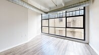 Located in the heart of downtown Dayton, Ohio, Unit 322 at 35 S Saint Clair St offers a compelling blend of industrial character and modern finishes. The residence spans a single floor with a thoughtfully arranged layout that maximizes its generous footprint.

The space is immediately distinguished by its exposed ductwork running along the ceilings, structural concrete beams, and durable wood-look flooring throughout. The open-concept kitchen features gray cabinetry, light countertops, a full suite of appliances including a stainless steel range, microwave, black refrigerator, and dishwasher, all framed by a peninsula that separates it from the living area. A hallway with a louvered closet door connects the main living spaces.

One of the most striking features is the floor-to-ceiling, black-framed industrial windows that flood the living area with natural light and offer views of the surrounding urban brick architecture. Exposed ductwork along the upper perimeter of this room reinforces the loft aesthetic.

The unit includes three bathrooms, each featuring dark-stained wood vanities with mirrors, light countertops, and shower/tub combinations. A walk-in closet with built-in wire shelving provides ample organized storage. The overall ambiance is modern-industrial, clean, and urban.