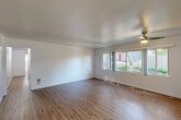 Located at 3500 Edison Street in San Mateo, CA, this single-story 2-bedroom, 1-bathroom home offers a functional and well-organized layout. The living room serves as the heart of the home, featuring warm hardwood-style flooring, crisp white walls, and a ceiling fan with light fixture. A wide set of windows floods the space with natural light and provides views of the surrounding greenery, creating a bright and welcoming atmosphere. The living room connects directly to the kitchen, which is outfitted with white shaker-style cabinetry, light countertops, a stainless steel undermount sink, and a window above the counter that brings in additional natural light. A stove is also present, completing the functional cooking space. Both bedrooms are finished with neutral carpet and feature windows with vertical blinds, allowing for adjustable natural light. The primary bedroom offers a generous footprint with a closet. A connecting hallway links the bedrooms to the shared full bathroom, which includes a tub-shower combination with grab bars, a curved shower rod, a window for ventilation, and a vanity with sink. The overall aesthetic is clean, neutral, and move-in ready.