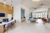 Located at 3784 West 88th Street in Hialeah, FL, this single-floor community clubhouse is a thoughtfully designed social hub spanning a generous footprint. The space makes an immediate impression with its dramatic double-height ceilings, floor-to-ceiling windows, and large-format light-toned tile flooring that flows throughout the main areas.

The welcoming reception lobby features a curved reception desk, warm wood wall paneling, and eye-catching sculptural pendant lighting. A bold, horizontally striped blue-and-white art installation serves as a striking focal point behind a floating wood credenza. Adjacent seating areas are furnished with curvaceous sofas and sculptural accent chairs, creating an inviting and contemporary atmosphere.

The two living areas each have a distinct character. One boasts a sweeping wall of tall black-framed windows offering panoramic views of the outdoor pool and patio, flooding the space with natural Florida light. The other features ocean-inspired wallcovering, integrated wood paneling with recessed screens, and warm hardwood flooring. A flexible lounge and dining area with a sliding barn door offers additional gathering space.

A connecting hallway with black-framed glass walls leads to additional amenities, including a fitness area. Throughout, the design palette of soft whites, natural wood tones, and coastal blues creates a cohesive, resort-like ambiance.