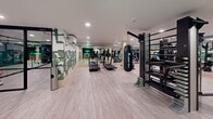 Located at 4722 Rainier Ave S in Seattle, WA, this fitness facility delivers a comprehensive workout environment across a generously sized single-floor space. The interior is thoughtfully designed with light wood-style flooring and wood-wrapped structural columns that lend warmth to an otherwise sleek, modern aesthetic. Recessed lighting throughout ensures consistent, bright illumination across the entire floor.

The main workout area is divided into distinct functional zones. A robust cardio section features treadmills, elliptical trainers, stationary bikes, and rowing machines arranged with ample space between equipment. The strength training zone offers an extensive dumbbell rack spanning a wide weight range, multiple weight machines, a cable system, and a hanging heavy bag for boxing training. Full-length mirrors line the walls, visually expanding the space and allowing users to monitor their form.

A stall bar and multi-functional rig add versatility for bodyweight and functional training. Mounted flat-screen televisions are positioned throughout the floor for entertainment. Exposed ductwork adds an industrial touch near the ceiling in select areas.

The entryway makes a striking first impression with a bold neon "Make It Happen" sign set against a dark feature wall, complemented by a bold green abstract mural that adds artistic character to the space. The overall ambiance is energetic, modern, and well-organized.