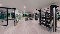 Located at 4722 Rainier Ave S in Seattle, WA, this fitness facility delivers a comprehensive workout environment across a generously sized single-floor space. The interior is thoughtfully designed with light wood-style flooring and wood-wrapped structural columns that lend warmth to an otherwise sleek, modern aesthetic. Recessed lighting throughout ensures consistent, bright illumination across the entire floor.

The main workout area is divided into distinct functional zones. A robust cardio section features treadmills, elliptical trainers, stationary bikes, and rowing machines arranged with ample space between equipment. The strength training zone offers an extensive dumbbell rack spanning a wide weight range, multiple weight machines, a cable system, and a hanging heavy bag for boxing training. Full-length mirrors line the walls, visually expanding the space and allowing users to monitor their form.

A stall bar and multi-functional rig add versatility for bodyweight and functional training. Mounted flat-screen televisions are positioned throughout the floor for entertainment. Exposed ductwork adds an industrial touch near the ceiling in select areas.

The entryway makes a striking first impression with a bold neon "Make It Happen" sign set against a dark feature wall, complemented by a bold green abstract mural that adds artistic character to the space. The overall ambiance is energetic, modern, and well-organized.