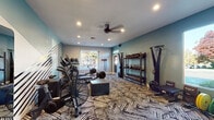 Located at 3400 S Lowell Blvd in Denver, Colorado, this fitness center is a thoughtfully designed, single-floor workout facility that delivers a comprehensive exercise experience. The space is defined by its bold, modern aesthetic, featuring teal accent walls paired with a striking geometric striped mural bearing the motivational phrase "GET FIT." A patterned carpet with an abstract design covers the floor throughout, adding visual energy to the environment. Recessed lighting and a ceiling fan ensure the space remains well-lit and comfortable during workouts. Natural light filters in through multiple windows, creating an inviting atmosphere. The facility is comprehensively equipped to support a wide range of training styles. A full power rack with barbells and bumper plates anchors the strength training area, accompanied by a tiered dumbbell rack and a full set of kettlebells for free weight work. Functional training accessories, including resistance bands and wall-mounted attachments, provide additional versatility. For cardio, the space houses air bikes, Concept2 rowing machines, and a treadmill with an interactive display. Medicine balls are neatly stored on wall-mounted racks. A dedicated entry door with a transom window above completes the layout, making this fitness center a well-rounded and energetic space for residents and users seeking a quality workout environment.