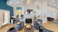Located at 800 Walden Dr in Wilmington, NC, this single-story community amenity space is thoughtfully designed to offer both comfort and functionality. The lounge area serves as the heart of the space, anchored by a sleek tile-surround fireplace with a wall-mounted television above it. Plush gray armchairs and a stylish coffee table create an inviting seating arrangement, while decorative gold disc wall art and colorful abstract paintings add a curated, contemporary aesthetic. Recessed lighting and wood-look flooring complement the neutral tones throughout.

Adjacent to the lounge is a vibrant game and social room, distinguished by bold teal accent walls, dramatic vaulted ceilings, and skylights that draw in natural light. Multiple sets of French doors open to the outdoors, enhancing the sense of openness. A billiards table anchors one end of the room, while a large wall-mounted screen and additional lounge seating make it ideal for gatherings.

The kitchen is well-appointed with charcoal gray cabinetry, white subway tile backsplash, light countertops, and stainless steel appliances including a full-size refrigerator and dishwasher. French doors in the kitchen area provide direct outdoor access, further connecting the interior to the surrounding environment.