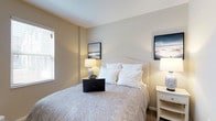 Located at 1655 Gilmore Park Ave in Columbus, Ohio, this single-floor residence offers a calm and comfortable living environment designed with simplicity and function in mind. The bedroom serves as a restful retreat, showcasing warm neutral wall tones that create a soothing, welcoming atmosphere. Soft carpeting underfoot adds to the sense of comfort throughout the space. Natural light filters in through a window dressed with classic white blinds, brightening the room and enhancing its airy feel. The room comfortably accommodates a full-sized bed with an upholstered headboard, flanked by matching nightstands and elegant table lamps that provide warm, ambient lighting. Tasteful framed artwork adorns the walls, adding a subtle decorative touch that complements the understated color palette. The clean, uncluttered layout of the bedroom reflects a thoughtful approach to interior design, prioritizing ease of movement and a tranquil ambiance. The overall aesthetic of this residence leans toward quiet sophistication, making it a welcoming and functional home in a residential Columbus neighborhood.