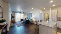 Located at 277 W 13490 S in Draper, Utah, this single-floor residence offers a thoughtfully designed open-concept layout with contemporary finishes and scenic outdoor views. The living area is anchored by rich hardwood-style flooring, a ceiling fan, and large sliding glass doors that open to a private balcony overlooking the surrounding landscape — flooding the space with abundant natural light. The kitchen is well-appointed with light wood cabinetry, granite countertops, a subway tile backsplash, stainless steel appliances including a refrigerator, dishwasher, and range, as well as a center island with bar seating. The primary bedroom is a serene retreat featuring plush carpeting, large windows with blinds and curtain panels, and direct access to a private en-suite bathroom. The primary bath includes a granite-topped vanity with light wood cabinetry and a walk-in closet. A second bedroom also offers generous natural light through sizable windows. The full secondary bathroom features a granite vanity, hardwood-style flooring, and a full tub-shower combination. Throughout the residence, a neutral color palette, recessed lighting, and clean architectural lines create a cohesive, modern ambiance suited to comfortable everyday living.