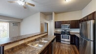 Located at 3410 5th Ave NE in Watford City, North Dakota, this single-floor, three-bedroom, three-bathroom home offers a practical and well-organized layout. The open-concept kitchen is a standout feature, equipped with rich dark cabinetry, granite-style countertops, stainless steel appliances including a range, microwave, refrigerator, and dishwasher, and a double-basin sink set into a peninsula that overlooks the living area. Hardwood-style flooring runs throughout the main living and kitchen spaces, while the bedrooms are finished with plush carpeting for added comfort. Ceiling fans are present in the living area and bedrooms, contributing to a comfortable atmosphere year-round. Each bedroom offers natural light through framed windows with exterior views, and baseboard heating ensures warmth during colder months. The bathrooms feature dark vanity cabinetry with white countertops, and at least one includes a full tub-shower combination. A dedicated in-unit laundry room houses a full-size washer and dryer with an overhead shelf. Four closets distributed throughout the home provide generous storage. The space maintains a clean, neutral palette throughout, creating a bright and functional living environment.