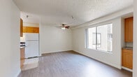 Located on Laurel Canyon Boulevard in North Hollywood, Los Angeles, this 2-bedroom, 1-bathroom unit offers a practical and efficient single-floor layout. The open living area features light-toned laminate wood flooring, crisp white walls, and a textured ceiling with a ceiling fan and light fixture, contributing to a bright and airy feel. A large sliding window allows natural light to flow into the space and provides views of the surrounding building exterior. The living area flows directly into the kitchen, which is finished with light tile flooring, warm honey-toned wood cabinetry, granite-look countertops, a stainless sink, and a white refrigerator — offering a functional and tidy cooking space. The two bedrooms continue the laminate flooring theme, each featuring ceiling fans and large windows that bring in ample natural light. The primary bedroom includes a wall-mounted HVAC unit for individual climate control. The full bathroom is clean and simply appointed with tile flooring, a white vanity with under-cabinet storage, and a shower-tub combination. Overall, the unit presents a clean, no-frills aesthetic well-suited for comfortable everyday living in a central Los Angeles location.
