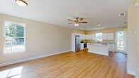 Located at 216 S Florida Ave in DeLand, Florida, this two-story home offers 4 bedrooms and 3 bathrooms across two well-proportioned floors. The main level hosts an open-concept living, dining, and kitchen area bathed in natural light, with warm-toned walls and light hardwood flooring that flows seamlessly throughout. The kitchen is a standout feature, equipped with white shaker cabinetry, stone countertops, a central island, stainless steel appliances including a refrigerator, range, and dishwasher, and a pantry for added storage. Built-in wall shelving and ceiling fans with lighting add functional charm to the living area, which also provides direct access to the exterior. The upper floor accommodates all four bedrooms, including a spacious primary bedroom, along with a hallway connecting the rooms and closets. Three full bathrooms serve the home, each finished with clean white fixtures; one features a tub-shower combination with a window for natural light, while another includes a wide vanity with stone countertops. A dedicated laundry room and utility space add everyday convenience. Throughout the home, consistent light wood flooring, neutral warm paint tones, recessed lighting, and white trim create a cohesive, modern aesthetic.