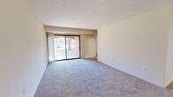 Located at 7509 Mandan Rd, Unit T3 in Greenbelt, Maryland, this two-bedroom, two-bathroom residence offers a practical and comfortable single-floor layout. The spacious living room is highlighted by plush wall-to-wall carpeting, neutral-toned walls with a textured ceiling, and a sliding glass door that fills the room with natural light and provides views of the landscaped outdoor surroundings. The galley-style kitchen is well-appointed with warm wood cabinetry, dark speckled countertops, a double sink, and white appliances including a range and refrigerator, all set over hardwood-style flooring. The kitchen opens conveniently to the main living area. The generously sized primary bedroom offers ample space along with dual closets for storage. The second bedroom features carpeting and a window allowing natural light. Three closets throughout the unit provide abundant storage. Both bathrooms are finished with wood-toned vanity cabinetry, white tile tub-shower surrounds, and hardwood-style flooring, maintaining a clean, functional aesthetic. The unit's neutral color palette and efficient floor plan make it a versatile and move-in ready home in the heart of Greenbelt, MD.