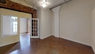 This 2-bedroom, 2-bathroom unit showcases a distinctive loft-inspired aesthetic rooted in industrial design. Polished concrete floors flow throughout the living spaces, reflecting light and lending a sleek, urban character to every room. Exposed metal ductwork and track lighting along the ceilings reinforce the industrial sensibility, while elevated transom-style interior windows allow light to pass between spaces, adding architectural interest and a sense of openness.

The main living area is generously proportioned, featuring high ceilings and clean white walls that contrast with the raw, textural elements present throughout. A French door with divided glass panes connects rooms, adding a refined touch amid the industrial backdrop. One bedroom retains the soaring ceiling height, with transom windows above and a double-door closet providing practical storage.

Exposed brick detailing in one of the rooms adds warmth and character, grounding the space with historic charm. The kitchen is outfitted with white shaker-style cabinetry, dark granite countertops, a white subway tile backsplash, and stainless steel appliances including a range, over-the-range microwave, and refrigerator. An in-unit washer and dryer are also included.

Both bathrooms mirror each other in design, featuring tile flooring, white vanities with dark granite countertops, and tub-shower combinations.