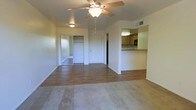 This single-floor residence offers a practical and comfortable layout designed for easy living. The main living area is spacious and open, featuring a combination of warm hardwood-style flooring and plush carpeting that defines distinct zones within the space. A ceiling fan with integrated lighting anchors the room, providing both airflow and ambient illumination.

A pass-through counter connects the living area to the kitchen, which is outfitted with light wood cabinetry, a built-in oven, and ample counter space. The open sightlines between the two areas create a connected, sociable atmosphere ideal for everyday use.

The bedroom is accessible directly from the living area and includes a generously sized closet with sliding mirrored doors, adding both storage and a sense of depth to the room. An additional door off the living space provides access to further areas of the unit.

Neutral wall tones throughout keep the interior feeling bright and clean, while HVAC vents are thoughtfully placed to ensure consistent climate control. The overall design is straightforward and functional, making efficient use of the available footprint while maintaining a welcoming, livable ambiance.