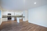 Located at 5196 Golden Rd in Pleasanton, CA, this well-appointed 2-bedroom, 1-bathroom single-story home offers a thoughtfully designed layout with clean finishes throughout. The open kitchen and dining area is a standout feature, showcasing bright white shaker cabinetry extending to the ceiling, dark quartz countertops, a peninsula island, and a full suite of stainless steel appliances including a range, microwave, dishwasher, and refrigerator. Warm hardwood flooring runs through the kitchen, dining, and living areas, lending a cohesive and inviting feel. The living room is filled with natural light courtesy of a large sliding glass door and adjacent window, which open to a private balcony overlooking mature trees. Both bedrooms feature plush neutral carpeting and windows that bring in additional natural light. The primary bedroom is generously sized and includes mirrored sliding closet doors. The second bedroom also features a window with greenery views. Multiple closets throughout the home provide ample storage. The full bathroom is outfitted with a tub/shower combination, a dark-finished vanity, and hardwood-style flooring. A dedicated laundry area and two hallways complete this efficiently organized and move-in-ready home.