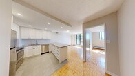 This efficiently designed one-bedroom, one-bathroom unit makes excellent use of its compact footprint across a single floor. Warm parquet flooring runs throughout the main living areas and bedroom, lending a classic character to the space. The open-concept kitchen flows directly into the living room, creating a cohesive and functional layout. The kitchen is well-appointed with white shaker-style cabinetry, stainless steel appliances including a refrigerator, stove, microwave, and dishwasher, recessed lighting, and a peninsula that provides additional counter space and separates the kitchen from the living area. Tile flooring grounds the kitchen zone distinctly within the open plan. The living room benefits from generous natural light through a sliding glass door that opens onto a balcony, offering views of surrounding greenery and the outdoors. Baseboard heating units are present throughout the unit. The bedroom is a comfortable, well-proportioned room featuring parquet flooring, a window that invites natural light, and a built-in sliding door closet. The bathroom is finished with clean white subway tile surrounding a bathtub and shower combination, complemented by chrome fixtures for a crisp, modern feel.