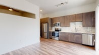 Located at 4811 S Niagara St in Denver, Colorado, this single-floor residence offers a clean, contemporary design throughout. The open-concept layout is anchored by a well-appointed kitchen featuring rich, medium-toned wood cabinetry extending floor to ceiling, a striking marble-effect tile backsplash, white quartz countertops, and a full suite of stainless steel appliances including a refrigerator, electric range, microwave, and dishwasher. Track lighting overhead provides focused illumination across the workspace. Light-toned luxury vinyl plank flooring flows seamlessly throughout the unit, adding warmth and visual continuity. A large sliding glass door in the living area opens to a private balcony, flooding the space with natural light and offering views of the surrounding Denver neighborhood. A unique architectural detail — a rectangular pass-through opening in the upper wall — connects adjacent spaces and adds an interesting design element, while a ceiling fan is visible through the opening in the bedroom area. The bathroom maintains the same design language as the rest of the unit, with wood-look tile flooring, a dark-cabinetry vanity with white countertop, and a tiled walk-in shower. The overall aesthetic is modern and cohesive, emphasizing clean lines, neutral tones, and quality finishes throughout.