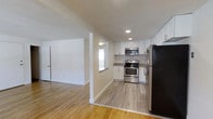 Located at 1650 West Chester Pike in West Chester, Pennsylvania, this single-floor space offers a clean, modern aesthetic with a thoughtfully designed layout. The kitchen is a standout feature, showcasing white shaker-style cabinetry, granite-look countertops, and a full suite of stainless steel appliances including a gas range, built-in microwave, and a large refrigerator. Recessed lighting illuminates the kitchen area, complementing the natural light that filters in through a window above the counter. The kitchen flows seamlessly into the adjacent living area, creating an open and connected feel throughout the space. Light hardwood flooring extends continuously across both areas, adding warmth and visual cohesion to the interior. The walls are finished in a crisp, neutral white, enhancing the bright and airy ambiance. A dedicated room with a door provides separation and privacy, offering functional versatility. The overall design balances practicality with contemporary style, making this a well-appointed space in the heart of West Chester, PA.