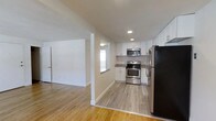 Located at 1650 West Chester Pike in West Chester, Pennsylvania, this single-floor space offers a clean, modern aesthetic with a thoughtfully designed layout. The kitchen is a standout feature, showcasing white shaker-style cabinetry, granite-look countertops, and a full suite of stainless steel appliances including a gas range, built-in microwave, and a large refrigerator. Recessed lighting illuminates the kitchen area, complementing the natural light that filters in through a window above the counter. The kitchen flows seamlessly into the adjacent living area, creating an open and connected feel throughout the space. Light hardwood flooring extends continuously across both areas, adding warmth and visual cohesion to the interior. The walls are finished in a crisp, neutral white, enhancing the bright and airy ambiance. A dedicated room with a door provides separation and privacy, offering functional versatility. The overall design balances practicality with contemporary style, making this a well-appointed space in the heart of West Chester, PA.