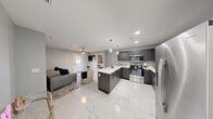 This thoughtfully designed 2-bedroom, 2-bathroom residence offers a cohesive modern aesthetic throughout, anchored by striking marble-look porcelain tile flooring that flows seamlessly across the entire unit. The open-concept kitchen is a standout feature, showcasing dark wood cabinetry, quartz countertops, a peninsula with bar seating, and a full suite of stainless steel appliances including a French door refrigerator, dishwasher, and range. Elegant pendant lighting adds a refined touch above the kitchen island, while the adjacent living area provides comfortable space for relaxing, complete with a ceiling fan and direct access to an outdoor balcony. Both bedrooms are finished in calming gray tones with ceiling fans and ample closet space; the primary bedroom benefits from natural light through a window with exterior views. Each bathroom is well-appointed, featuring marble-look tile flooring, dark vanity cabinetry, illuminated mirrors, and a tub-shower combination. A dedicated laundry room with a full-size washer and dryer adds everyday convenience. The overall ambiance is clean, contemporary, and functional, making this a highly practical and attractive living space.