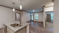 Located at 114 SE Douglas St in Lee's Summit, MO, this single-floor residence offers a thoughtfully designed open-concept layout with contemporary finishes throughout. The kitchen serves as the centerpiece of the living space, showcasing a large island with granite countertops, an undermount stainless steel sink, and elegant pendant lighting overhead. White shaker-style cabinetry lines the walls, complemented by a subtle tile backsplash and a full suite of stainless steel appliances, including a refrigerator, range, and over-the-range microwave. Hardwood-style flooring flows seamlessly through the main living areas, while crown molding with dark wood accents adds a refined architectural detail throughout. The living area is bright and open, benefiting from natural light through windows fitted with blinds. Bedrooms feature plush carpeting and generous natural light. The bathrooms are finished with granite-topped vanities, tile-surround showers, and accessibility-conscious grab bars for added convenience and safety. Recessed lighting and a neutral color palette contribute to a clean, modern ambiance that is both functional and inviting throughout the entire space.
