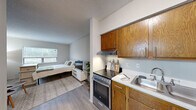 Located at 4700 Westgrove St in Raleigh, NC, this efficiently designed unit offers a well-organized single-floor layout that maximizes every square foot. The open-concept main living area serves as both bedroom and living space, featuring light wood-tone flooring, neutral gray walls, and a textured ceiling that together create a clean, modern aesthetic. A large window fills the room with natural light and provides a view of the surrounding greenery, enhancing the sense of openness. The space comfortably accommodates a full-sized bed, seating area, and media setup.

The kitchen is positioned along one wall and is defined by warm oak cabinetry both above and below the countertops, offering generous storage. It is equipped with a stainless steel refrigerator, an electric range with a ventilation hood, a double-basin sink, and light countertops — providing all essential cooking amenities in a compact, practical footprint.

The bathroom is accessed through a paneled white door and features a bright, clean design with a white vanity, a large mirror with overhead lighting, tiled flooring, and louvered cabinet doors that add a subtle classic detail. Overall, the unit presents a functional and well-maintained living space suited for individuals seeking an efficient home in Raleigh.