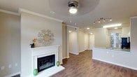 This single-floor Dallas residence offers a thoughtfully designed open-concept layout that seamlessly connects the living area to the kitchen and hallway beyond. The living room is anchored by a classic white-mantled fireplace, adding both warmth and architectural character to the space. Crown molding lines the ceilings throughout, lending an elegant, finished look to the interior.

Warm-toned hardwood flooring runs continuously across the main living areas, providing a cohesive and inviting aesthetic. A ceiling fan with integrated lighting serves the living room, while adjustable track lighting illuminates the kitchen area, ensuring well-lit spaces throughout. The kitchen features granite or stone countertops visible from the living area, hinting at quality finishes carried throughout the home.

Neutral, warm beige walls create a calm and versatile backdrop, complemented by recessed lighting in the hallway and adjoining spaces. Multiple interior doors are visible down the hallway, indicating well-defined private rooms beyond the open living area. The overall ambiance is clean, bright, and inviting, reflecting a residential design that balances comfort and style in a practical single-level floor plan situated in Dallas.