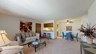 This single-floor residence offers a functional and comfortable layout designed for everyday living. The open-concept living and dining area forms the heart of the home, with plush carpeting, generous natural light from a large sliding glass door fitted with vertical blinds, and seamless flow between spaces. A ceiling fan with a light fixture overhead serves the dining area, which connects directly to the kitchen pass-through, adding a sense of openness and connectivity throughout.

The galley-style kitchen is efficiently designed with warm wood cabinetry lining both walls, offering ample storage and counter space. White appliances include an electric range, refrigerator, and dishwasher. A notable feature is the in-unit washer and dryer, conveniently integrated into the kitchen area. Light tile flooring completes the functional aesthetic.

The residence includes two bedrooms, each with soft carpeting and closet storage. One bedroom features a sliding double-door closet and a window providing natural light, while the primary bedroom offers additional space for a full dresser suite. The full bathroom includes an extended vanity with a wood-toned cabinet base, a wide mirror, tile flooring, and a shower-tub combination. A pass-through bar with seating connects the kitchen to the main living space, adding a casual dining option to this well-organized home.