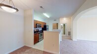 Located at 2000 Crossroads Manor Ct in Cary, NC, this single-floor residence offers a well-organized layout designed for comfortable everyday living. The kitchen is outfitted with warm wood cabinetry, tile flooring, a stainless steel range, microwave, and refrigerator, complemented by a breakfast bar that connects to the adjacent dining area. A pendant light fixture illuminates the dining space, which flows naturally into the living room. The spacious living room features plush carpeting, crown molding, a ceiling fan, and sliding glass doors that open to an outdoor patio with views of the surrounding community. The bedrooms are generously sized with soft carpeting, ceiling fans, and natural light provided by windows with blinds. One bedroom includes a walk-in closet with built-in shelving, offering excellent storage. The primary bathroom features a tiled walk-in shower with a glass door, a vanity with a vessel-style sink, and tile flooring. A second full bathroom includes a soaking tub and shower combination with white tile surround. The dedicated laundry room houses a full-size washer and dryer with overhead wire shelving and tile flooring, adding a practical convenience to the home.