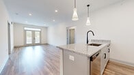 This well-appointed single-story home offers a thoughtfully designed layout across three bedrooms and two bathrooms, delivering a comfortable and modern living experience. The open-concept kitchen and living area serves as the heart of the home, featuring a large center island with granite countertops, a sleek matte black faucet, and stylish pendant lighting overhead. Gray shaker-style cabinetry pairs with stainless steel appliances to complete the contemporary kitchen aesthetic. Warm wood-look flooring flows throughout the main living areas, enhancing the bright, airy atmosphere created by recessed lighting and an abundance of natural light. The living room opens to a private outdoor space through elegant French doors topped with a transom window, offering scenic outdoor views. A central hallway lined with paneled doors connects the main spaces seamlessly. The bedrooms are finished with plush carpet flooring; the secondary bedrooms feature ceiling fans and generous windows, while the primary bedroom includes a walk-in closet outfitted with wire shelving for organized storage. The bathrooms are finished with granite-topped vanities, shaker cabinetry, and consistent matte black hardware, maintaining the home's cohesive modern design throughout.