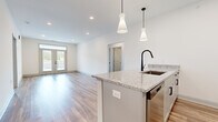 This well-appointed single-story home offers a thoughtfully designed layout across three bedrooms and two bathrooms, delivering a comfortable and modern living experience. The open-concept kitchen and living area serves as the heart of the home, featuring a large center island with granite countertops, a sleek matte black faucet, and stylish pendant lighting overhead. Gray shaker-style cabinetry pairs with stainless steel appliances to complete the contemporary kitchen aesthetic. Warm wood-look flooring flows throughout the main living areas, enhancing the bright, airy atmosphere created by recessed lighting and an abundance of natural light. The living room opens to a private outdoor space through elegant French doors topped with a transom window, offering scenic outdoor views. A central hallway lined with paneled doors connects the main spaces seamlessly. The bedrooms are finished with plush carpet flooring; the secondary bedrooms feature ceiling fans and generous windows, while the primary bedroom includes a walk-in closet outfitted with wire shelving for organized storage. The bathrooms are finished with granite-topped vanities, shaker cabinetry, and consistent matte black hardware, maintaining the home's cohesive modern design throughout.