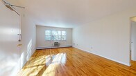 This single-floor residence offers a clean, well-maintained interior defined by warm, polished hardwood floors that extend throughout the living areas and bedrooms, reflecting natural light and lending the space a bright, welcoming character.

The spacious living room is a standout feature, offering generous proportions, crisp white walls, and multiple windows that bathe the room in sunlight. Baseboard heating and a wall-mounted air conditioning unit ensure year-round comfort. A dedicated dining area adjoins the living space, illuminated by a classic chandelier and a window with an outdoor view, making it an ideal spot for meals and gatherings.

The kitchen is equipped with warm honey-toned wood cabinetry, granite-style countertops, a tile backsplash, and white appliances including a gas range and over-the-range microwave. Tile flooring completes the practical and tidy aesthetic of the space.

The bedroom offers a tranquil retreat with the same gleaming hardwood floors and ample wall space. The bathroom is tastefully finished with large-format neutral ceramic tile surrounding a full soaking tub and shower combination, complemented by a white vanity with storage and a mirrored medicine cabinet above.

Throughout the residence, the design emphasizes clean lines, natural light, and functional simplicity.