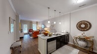 Located at Ascot Point in Asheville, NC, this well-appointed 2-bedroom, 2-bathroom residence offers a thoughtfully designed single-floor layout. The living room greets you with hardwood-style flooring, crown molding, and abundant natural light streaming through large windows and a glass door that opens to the outdoors. The kitchen is a standout feature, boasting a sweeping granite-topped breakfast bar with pendant lighting, dark espresso cabinetry, stainless steel appliances, and a subway tile backsplash — all flowing seamlessly into the dining area, which is highlighted by a chandelier overhead. The primary bedroom is generously sized, featuring plush carpet, a ceiling fan, a walk-in closet, and windows that bring in natural light. The second bedroom offers similar comfort with carpeted floors and a ceiling fan. Both bathrooms are finished with tile flooring, dark vanity cabinetry, and granite countertops. A spacious walk-in closet provides excellent storage. The neutral color palette and crown molding throughout lend a cohesive, polished ambiance to this Asheville residence.