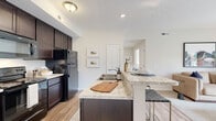 Located at 915 Galloway Rd in Galloway, Ohio, this single-floor, 1-bedroom, 1-bathroom residence offers a thoughtfully designed layout that maximizes both comfort and functionality. The open-concept kitchen and living room serve as the heart of the home, featuring rich dark-espresso cabinetry, granite-look countertops, and black appliances including a refrigerator, electric range, and microwave. A peninsula with bar seating provides additional prep space and a casual dining option, while wood-look flooring anchors the entire living and kitchen area. The living room is bright and inviting, benefiting from natural light streaming through a sliding glass door that opens to a private patio with outdoor views. The bedroom is a calm, carpeted retreat filled with natural light from a large window and includes a spacious closet with built-in shelving. The full bathroom features a tub-shower combination, tile flooring, and clean, neutral finishes. Additional conveniences include a dedicated laundry area, a utility room, multiple closets, and two pantry spaces for generous storage. A hallway connects the rooms with ease, rounding out this efficient and comfortable single-level home.