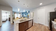 This thoughtfully designed 2-bedroom, 4-bathroom single-story residence offers a functional and stylish layout across a comfortable footprint. The open-concept kitchen and living area serves as the heart of the home, where a central island with granite countertops, a double-basin sink, and pendant lighting anchors the space. Rich dark wood cabinetry, a subway tile backsplash, and a full suite of stainless steel appliances — including a range, microwave, refrigerator, and dishwasher — complete the kitchen. Wood-look flooring flows seamlessly throughout, adding warmth and continuity. The living room features a bold accent wall in a deep teal-gray tone, creating a modern, inviting atmosphere with natural light from large windows. The primary bedroom offers a serene retreat with a bright window and ample closet space, while the second bedroom is equally comfortable. The primary bathroom includes a dual-sink vanity with granite countertops and a glass-enclosed walk-in shower with tile surround. A secondary bathroom features a soaking tub with tiled surround. The dedicated laundry room houses side-by-side washer and dryer units with overhead shelving for added storage. Two closets provide organizational convenience throughout.