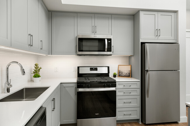 Apartments with modern kitchens featuring grey cabinetry, white quartz stone countertops, white tile backsplash, stainless steel appliances, and hard surface flooring - Avalon Monrovia