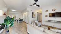 Located at 171 24th Street in Cocoa Beach, Florida, this well-appointed 2-bedroom, 2-bathroom single-story home offers a bright and comfortable layout finished with large-format tile flooring throughout. The open-plan living, dining, and kitchen area forms the heart of the home, where the living room features crown molding, a modern ceiling fan with light, and large windows dressed with stylish drapes that invite natural light. The kitchen is equipped with stainless steel appliances, two-tone cabinetry — white upper cabinets paired with light blue lower cabinets — dark stone countertops, and a tray ceiling with recessed lighting. The primary bedroom is generously sized, showcasing a ceiling fan, crown molding, a wall-mounted TV, and natural views through a windowed wall. Both bathrooms are fitted with glass-enclosed walk-in showers with tile surrounds and natural window light. A dedicated laundry room houses a full-size washer and dryer alongside overhead storage cabinets. Three closets provide ample storage throughout. The home also includes a balcony and a patio, offering outdoor spaces to enjoy the Florida climate. Crown molding and consistent tile flooring lend a cohesive, polished feel to the entire home.
