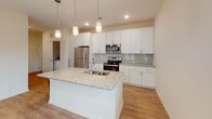 Located on Conductor Circle in Greer, South Carolina, this single-floor residence offers a clean, contemporary design with a thoughtful layout that balances open communal spaces with comfortable private quarters. The heart of the home is a well-appointed kitchen featuring crisp white shaker cabinetry, light granite countertops, a subway tile backsplash, and a full suite of stainless steel appliances including a refrigerator, electric range, microwave, and dishwasher. A large center island with an undermount sink and pendant lighting above serves as both a functional workspace and a natural gathering point, opening seamlessly into the adjacent living and dining areas. Light wood-style luxury vinyl plank flooring flows throughout the main living spaces, complementing the warm neutral tones of the walls. Natural light fills the living area through generously sized windows, while a glass door provides direct access to an outdoor area. The bedrooms are carpeted for comfort, each featuring ceiling fans and ample natural light through large windows. The bathroom includes a clean, tiled soaking tub and shower combination. A dedicated laundry area with an in-unit washer accommodates everyday convenience. Recessed lighting throughout gives the space a polished, modern finish.