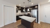 This single-floor residence in Castle Shannon, PA offers a thoughtfully designed layout with a cohesive blend of modern finishes and functional living spaces. The kitchen serves as a standout feature, showcasing rich dark cabinetry, granite countertops, and a central island with pendant lighting overhead. Stainless steel appliances, including a refrigerator, range, and microwave, complete the space, while durable hardwood-style flooring adds warmth and visual continuity. The open configuration of the kitchen allows for easy flow into adjacent living areas. Bedrooms are finished with plush wall-to-wall carpeting and neutral-toned walls, creating a calm and comfortable atmosphere. Natural light filters through window blinds, brightening each room. The bathrooms are cleanly appointed with classic black-and-white hexagon tile flooring, white subway tile surrounds, soaking tubs with shower combinations, and brushed nickel fixtures that provide a polished, contemporary look. The overall design emphasizes clean lines, neutral palettes, and practical finishes throughout, making this a well-appointed and move-in ready space in a convenient southwestern Pittsburgh suburb.