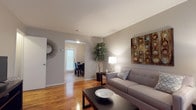 This two-story townhouse at Scott Gardens in Waterbury offers a well-organized layout across two floors, combining comfort and functionality throughout. The main level features a generously sized living room with warm hardwood floors, neutral gray walls, and an open flow into a separate dining area. Natural light filters in through windows fitted with blinds, creating a bright and welcoming atmosphere. The kitchen is equipped with ample oak cabinetry, dark countertops, a full-size refrigerator, and a range, all set atop easy-to-maintain tile flooring. The full bathroom on the upper level is clean and bright, featuring white tile walls, a vanity with a mirrored cabinet, and a tub-shower combination. The primary bedroom is a spacious retreat with gleaming hardwood floors, dual windows for natural light, and room for a full bedroom suite. The second bedroom, also featuring hardwood floors and a window, offers a comfortable and versatile space suitable as a guest room or home office. A staircase connects both levels, completing the practical two-floor layout of this townhouse. Throughout, the neutral color palette and consistent hardwood flooring create a cohesive and inviting living environment.