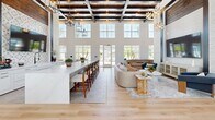 Located in Lady Lake, Florida, this beautifully designed single-floor space offers an impressive blend of modern elegance and relaxed, resort-style living. The soaring double-height ceilings, accented by exposed dark wood beams, immediately set a grand tone throughout the open interior.

The expansive living area is anchored by a dramatic floor-to-ceiling whitewashed brick feature wall, which houses a large flat-screen TV and is further adorned with decorative star-shaped pendant lights that add a warm, inviting glow. Plush seating arrangements and light hardwood flooring create an approachable yet refined atmosphere.

A generous game room area is highlighted by a full-size pool table, complemented by a circular chandelier and elegant wall sconces. An intricate patterned tile accent framed within the brick wall adds an artistic focal point to this zone.

A long marble-topped island with bar seating serves as both a functional and aesthetic centerpiece, ideal for gathering. Rows of oversized windows and glass doors flood the entire space with natural light and offer views of the surrounding outdoors.

A wide, light-filled corridor with additional seating connects areas seamlessly and leads toward further amenities. Throughout, the consistent use of light hardwood floors, crisp white walls, and curated furnishings creates a cohesive, upscale ambiance.