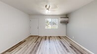 Located at 1950 North 43rd Avenue in Phoenix, Arizona, this efficiently designed single-floor unit makes smart use of its intimate footprint. The main living area welcomes natural light through a large window fitted with vertical blinds, offering views of the surrounding outdoor greenery. Light wood-look flooring flows throughout, complementing the neutral gray-and-white color palette that lends the space a clean, modern feel. A ceiling fan with integrated lighting provides both comfort and illumination in the main room.

The kitchen is thoughtfully appointed with light gray shaker-style cabinetry, a stainless steel sink, and a stainless steel refrigerator. A mosaic tile backsplash in gray tones adds a stylish accent, tying the space together with a contemporary touch.

The bathroom features a full tub-shower combination with floor-to-ceiling large-format gray tile surround and a built-in niche for storage. A white vanity with an integrated sink basin, a sizeable wall mirror, and light flooring complete the bathroom's clean aesthetic. Adjacent to the bathroom, a walk-in closet with built-in shelving and hanging rods provides practical storage. Throughout the unit, consistent finishes and a bright, neutral palette create a cohesive and inviting atmosphere.