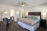 Located at 4821 W Century Blvd in Inglewood, California, this single-floor unit offers a thoughtfully designed layout that maximizes functionality and comfort. The bedroom serves as the central living space, featuring light wood-look flooring, a ceiling fan with integrated lighting, and a wall-mounted flat-screen TV. A large window allows natural light to fill the room, while a wall-mounted PTAC unit provides climate control. The bedroom is furnished with a king-sized bed accented by vibrant, colorful bedding, flanked by nightstands with table lamps, and complemented by a matching wood dresser — creating a warm and inviting atmosphere. A dedicated workspace with a desk and chair adds practical versatility to the room. The kitchen is bright and modern, outfitted with white shaker-style cabinetry, light stone countertops, a classic white subway tile backsplash, a stainless steel sink, and white appliances including a gas range and over-the-range microwave. The bathroom is clean and contemporary, finished with large-format white wall tiles, light wood-look flooring, and a glass-enclosed walk-in shower, offering a spa-like simplicity. Throughout the unit, the consistent use of light tones and wood-look flooring creates a cohesive and comfortable environment.